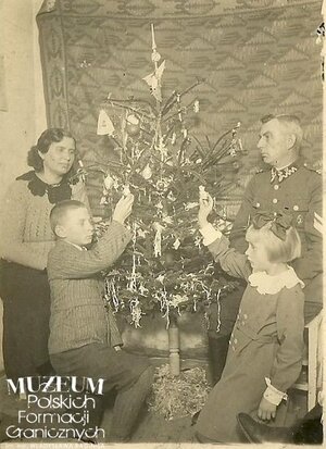 1. Tytuł tematu: Święta Bożego Narodzenia 
2. Opis obrazu: strażnik Adam Filipowiak z rodziną
3. Data wydarzenia:~1937r.
4. Osoby widoczne: strażnik  Adam Filipowiak  z Placówki Straży Granicznej Kaczyce (komisariat SG Zebrzydowice), żona Maria (z d. Morawska) ,syn Władysław, córka Wanda
5. Hasła przedmiotowe:  Straż Graniczna, życie rodzinne
6. Opis techniczny: 8x6 cm, oryginał, czarnobiałe
7. Autor: brak danych
8. Miejsce przechowywania/właściciel: Władysław Filipowiak
