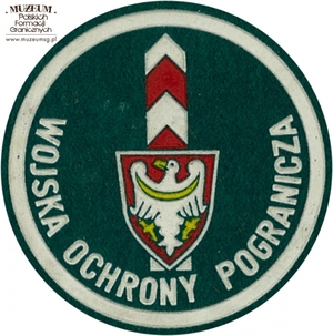 1. Nazwa własna: naszywka organizacyjna Łużyckiej Brygady  Wojsk Ochrony Pogranicza
2. Charakterystyka przedmiotu: okrągła plakietka (o średnicy 6,6 cm)  wykonana z filcu na podkładzie płóciennym. Obwiedziona białym paskiem,  w dolnej części półkoliście napis „Wojska Ochrony Pogranicza”. W centrum  pola logo jednostki organizacyjnej – na czerwonej tarczy herbowej  biały orzeł , w tle słup graniczny. Noszona na prawym przedramieniu  marynarki i płaszcza munduru wyjściowego
3. Czas powstania: lata 80. XX w.
4. Hasła przedmiotowe: Wojska Ochrony Pogranicza, umundurowanie
5. Miejsce przechowywania/właściciel: Śląski Oddział Straży Granicznej  w Raciborzu