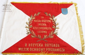 1.Nazwa własna: sztandar Łużyckiej Brygady Wojsk Ochrony Pogranicza
2.Charakterystyka przedmiotu: płat wykonany z jedwabnego rypsu (130 x 100 cm),barwy biała i czerwona ułożone zostały w cztery trójkąty, na stronie głównej pośrodku znajduje się orzeł bez korony, otoczony złotymi gałązkami wawrzynu. Na stronie odwrotnej - w centrum znajduje się dewiza „Za naszą ojczyznę Polską Rzeczpospolitą Ludową” otoczona złotym wieńcem wawrzynowym. Poniżej (na czerwonym tle) umieszczony jest napis: „8 Łużycka Brygada Wojsk Ochrony Pogranicza”. W górnym prawym rogu znajduje się plakietka fundatorów sztandaru o następującej treści „Społeczeństwo powiatów Lubań Śląski, Bolesławiec, Jelenia Góra, Lwówek Śląski, Zgorzelec i miasto  Jelenia Góra”. 
3.Czas powstania: 1963 r.
4.Hasła przedmiotowe: Wojska Ochrony Pogranicza, sztandary
5.Miejsce przechowywania/ właściciel: Sala Tradycji Ośrodka Szkoleń Specjalistycznych SG w Lubaniu
