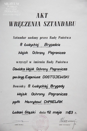 1.Tytuł: akt wręczenia sztandaru 8 Łużyckiej Brygadzie Wojsk Ochrony Pogranicza
2.Treść: akt wręczenia sztandaru przez gen. bryg. Eugeniusza Dostojewskiego, dowódcy WOP ppłk. dypl. Henrykowi Chmielakowi, dowódcy Łużyckiej Brygady WOP
3.Hasło przedmiotowe: Wojska Ochrony Pogranicza, sztandary
4.Wytwórca: Dowództwo WOP
5.Czas powstania: 12.05.1963 r.
6.Miejsce sporządzenia: Polska, Warszawa
7.Materiał i technika wykonania: papier, druk maszynowy  wypełniony pismem odręcznym
8.Wymiary: 37,5 x 29,5 cm
9.Stan zachowania: bardzo dobry
10.Miejsce przechowywania/ właściciel: Sala Tradycji Ośrodka Szkoleń  Specjalistycznych SG w Lubaniu