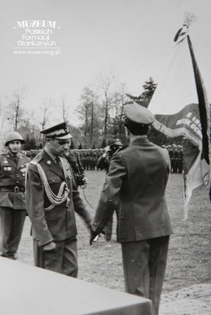 1.Tytuł tematu: uroczystość wręczenia sztandaru Łużyckiej Brygadzie Wojsk Ochrony Pogranicza
2.Opis obrazu: przekazanie sztandaru przez gen. bryg. Eugeniusza Dostojewskiego ppłk. dypl. Henrykowi Chmielakowi
3.Data wydarzenia: 12.05.1963 r.
4.Osoby widoczne: dowódca WOP gen. bryg. Eugeniusz Dostojewski (w środku),dowódca Łużyckiej Brygady WOP ppłk dypl. Henryk Chmielak (pierwszy od prawej)
5.Hasła przedmiotowe: Wojska Ochrony Pogranicza, sztandary
6.Opis techniczny: 12 x 18 cm, oryginał, czarnobiałe
7.Autor: brak danych
8.Miejsce przechowywania/właściciel: Sala Tradycji Ośrodka Szkoleń  Specjalistycznych SG w Lubaniu