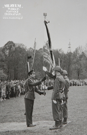 1.Tytuł tematu:  uroczystość wręczenia sztandaru Łużyckiej Brygadzie Wojsk Ochrony Pogranicza
2.Opis obrazu: przekazanie sztandaru przez ppłk. dypl. Henryka Chmielaka pocztowi sztandarowemu
3.Data wydarzenia: 12.05.1963 r.
4.Osoby widoczne: dowódca Łużyckiej Brygady WOP ppłk dypl. Henryk Chmielak(pierwszy z lewej)
5.Hasła przedmiotowe: Wojsk Ochrony Pogranicza, sztandary
6.Opis techniczny: 12 x 18 cm, oryginał, czarnobiałe
7.Autor: brak danych
8.Miejsce przechowywania/właściciel: Sala Tradycji Ośrodka Szkoleń  Specjalistycznych SG w Lubaniu