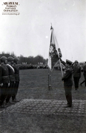 1. Tytuł tematu: wręczenie sztandaru
2. Opis obrazu:  płk Roman Wasilkowski przekazuje sztandar pocztowi  Pomorskiej Brygady Wojsk Ochrony Pogranicza
3. Data wydarzenia: 1963 r.
4. Osoby widoczne: płk Roman Wasilkowski, dowódca Pomorskiej Brygady WOP  (ze sztandarem)
5. Hasła przedmiotowe: Wojska Ochrony Pogranicza, sztandary
6. Opis techniczny: oryginał, czarnobiałe
7. Autor: brak danych
8. Miejsce przechowywania/właściciel: Zbigniew Nowicki